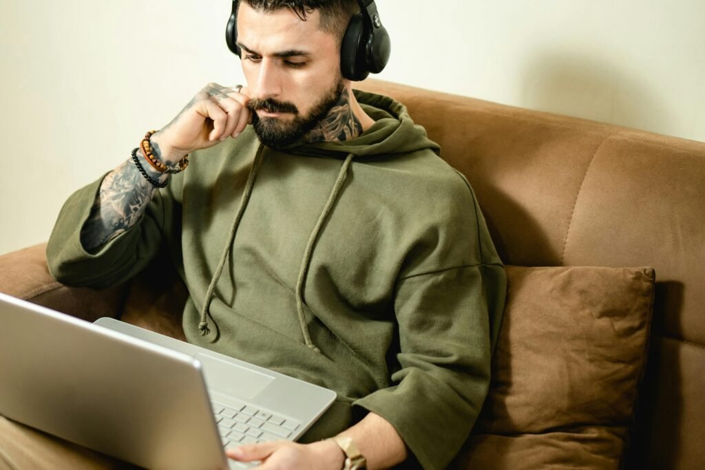 A person wearing high-quality headphones, deeply focused on their computer screen in a dimly lit room